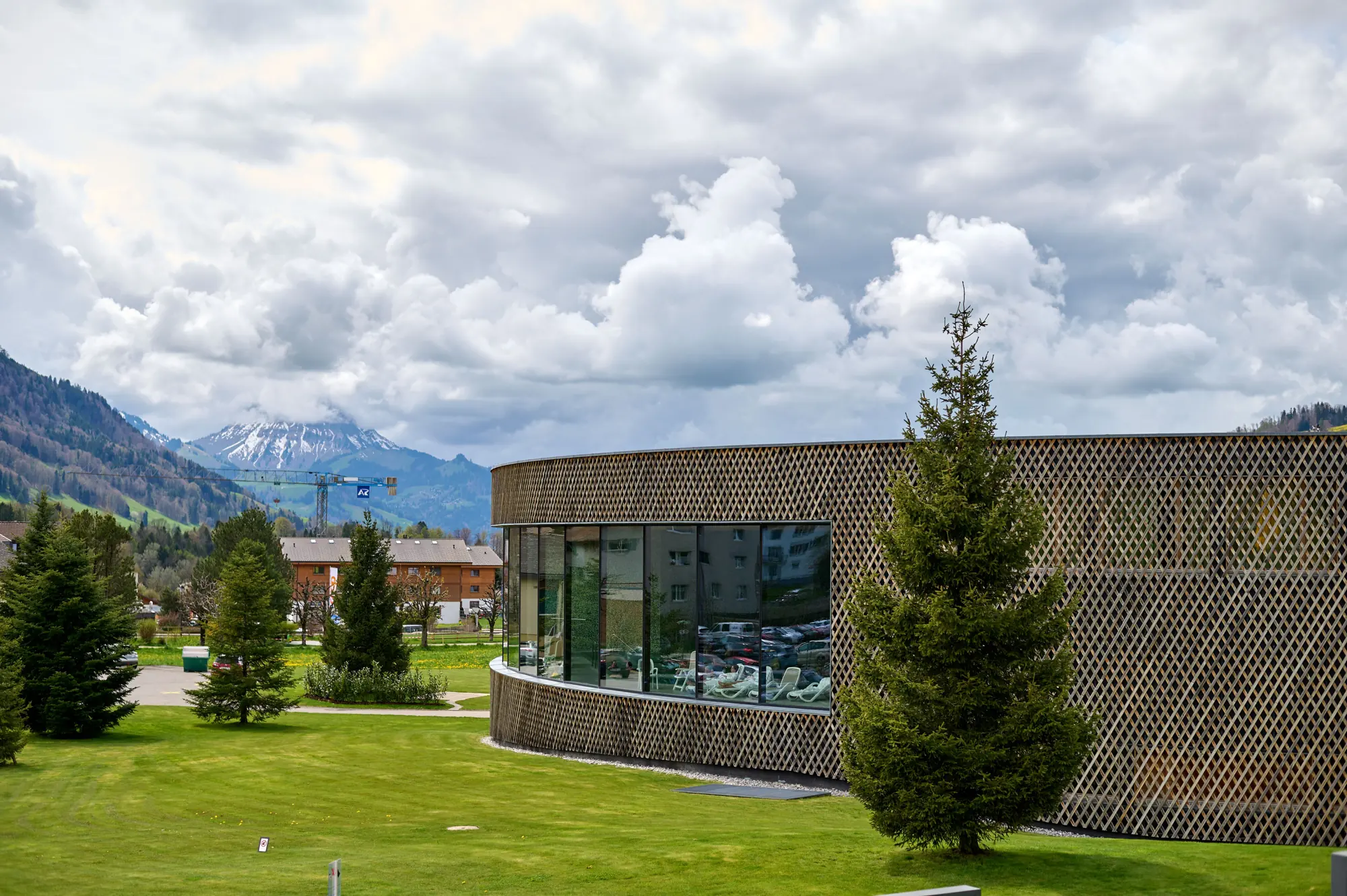 Zeitgenössisches Gebäude mit Holzfassade vor grünen Wiesen und Bergen